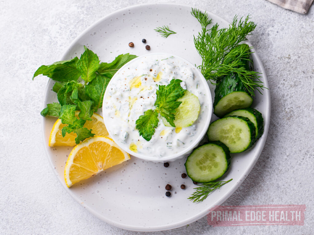Keto tzatziki sauce on a white plate with cucumbers and lemon.