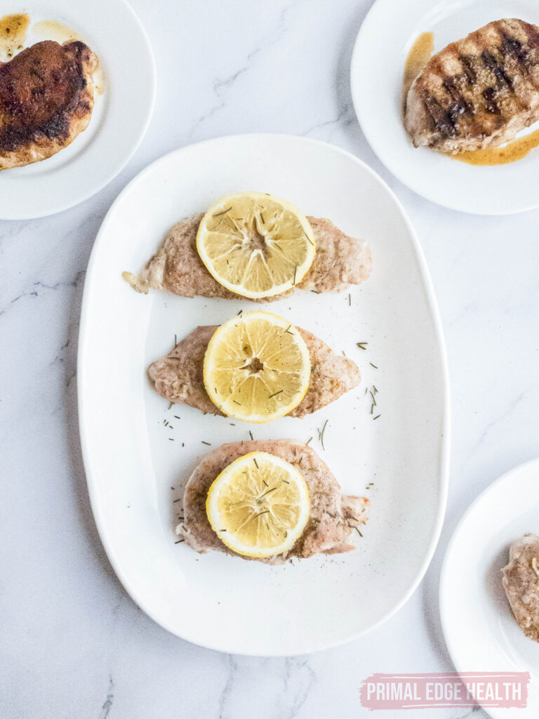 three lemon pork chops on a white plate with a grilled pork chop and fried pork chop in the background