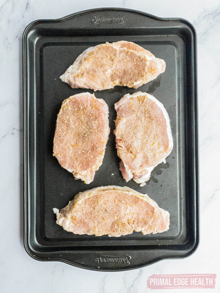 Four seasoned raw pork chops on a baking tray.
