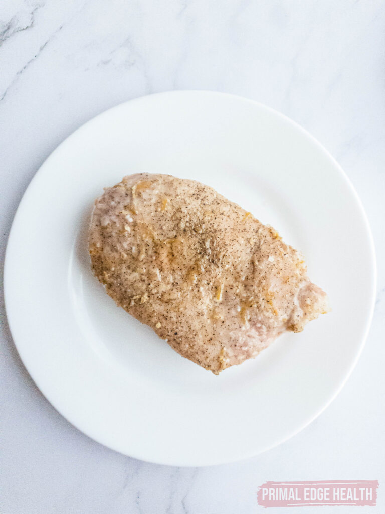 A seasoned, chicken breast on a white plate.