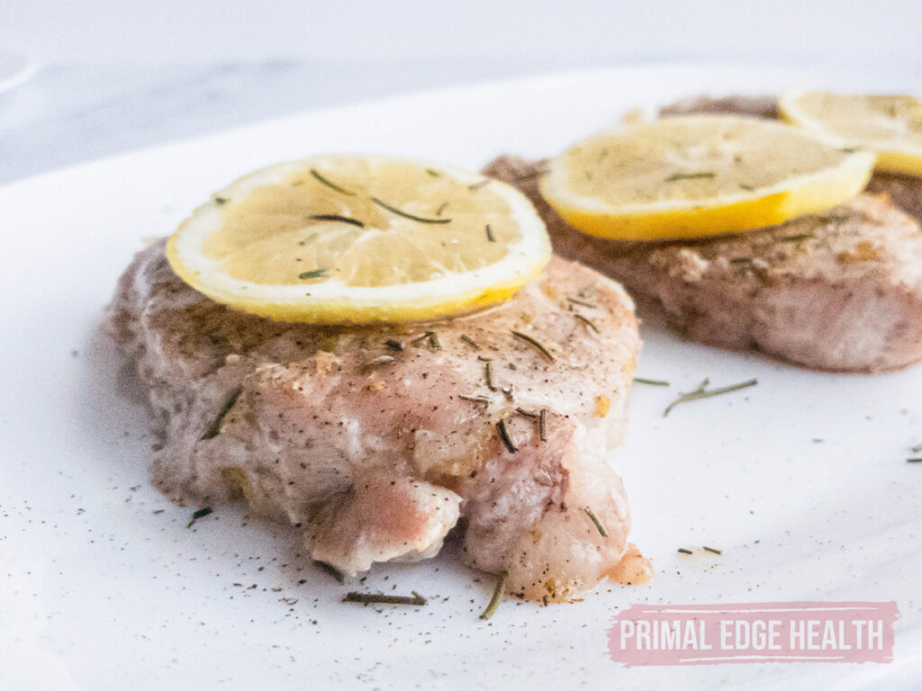 Pork chops topped with lemon slices and herbs on a white plate.