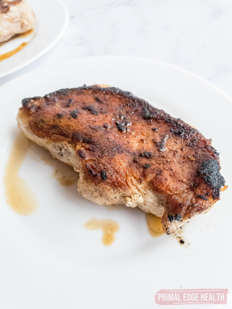 Cooked pepper pork chop on a white plate with visible char marks.