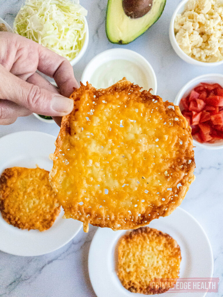 hand holding a cheese tostada shell with mexican ingredients in the background