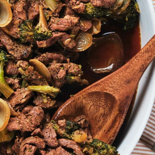 A close-up image of a keto beef and broccoli stir-fry in a white dish with a wooden spoon.