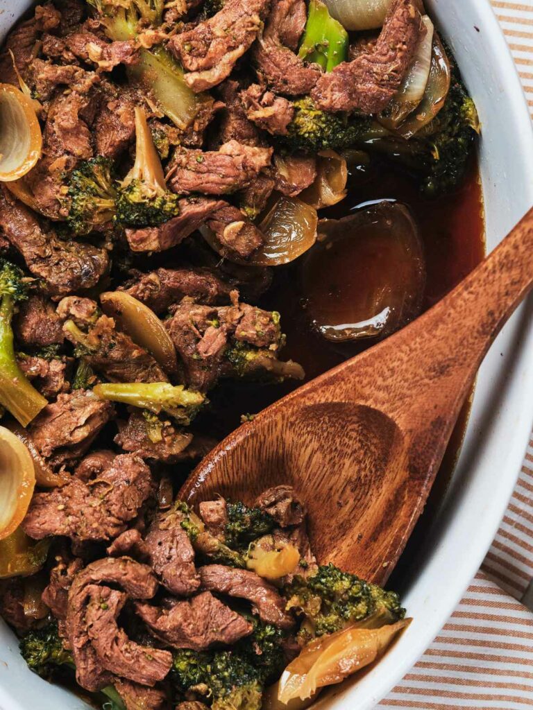 A close-up image of a keto beef and broccoli stir-fry in a white dish with a wooden spoon.