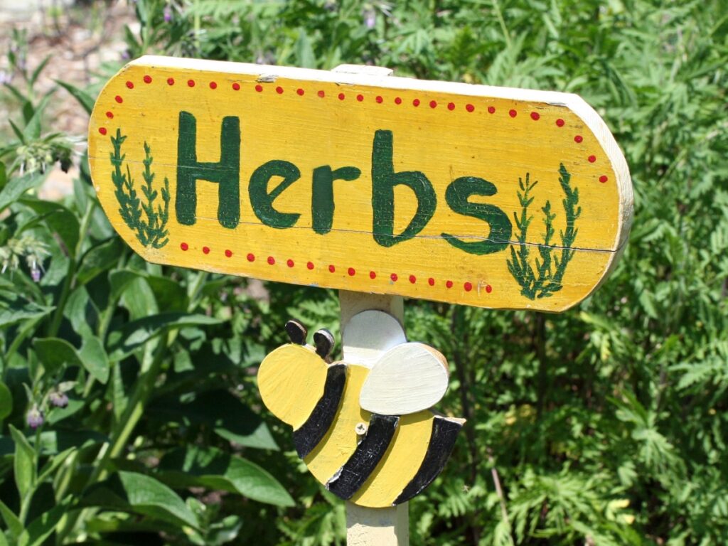 A yellow wooden herbs sign with painted bee.