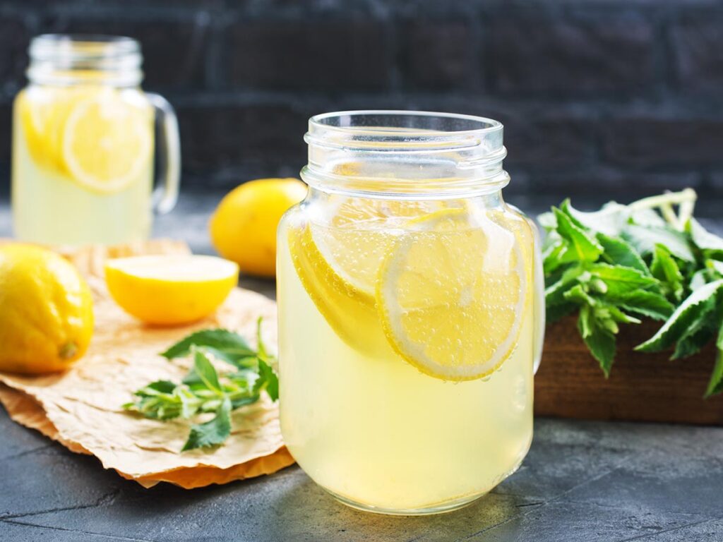 Lemonade in glass with mint in background.