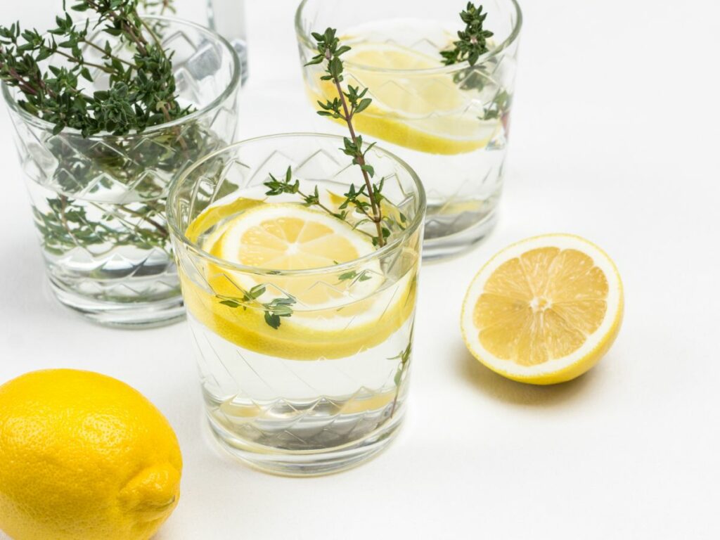 A glass of lemon water with herbs.