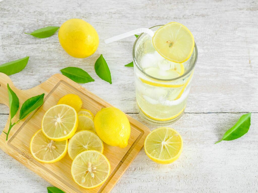 A glass of lemon water and lemon slices on a wooden board.