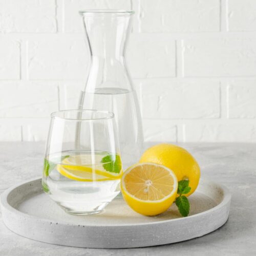 A pitcher and a glass of lemon water and fresh cut lemon on a tray.