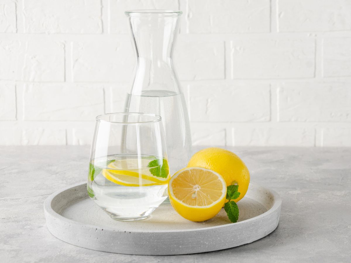 A pitcher and a glass of lemon water and fresh cut lemon on a tray.