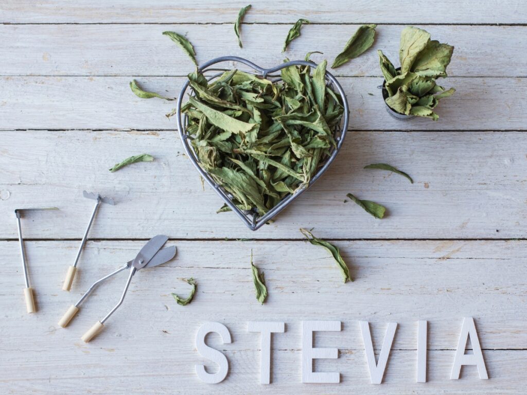 Dried stevia plant leaves in a heart-shaped container, with "stevia" spelled out below.