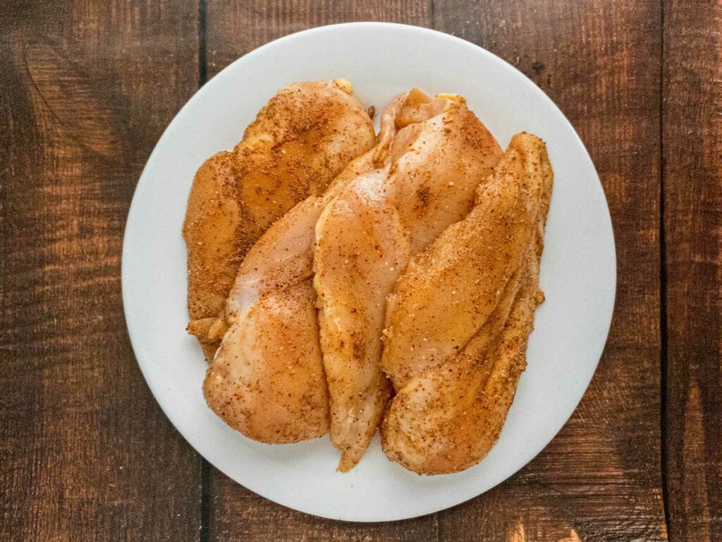 Seasoned raw chicken breasts on a white plate.