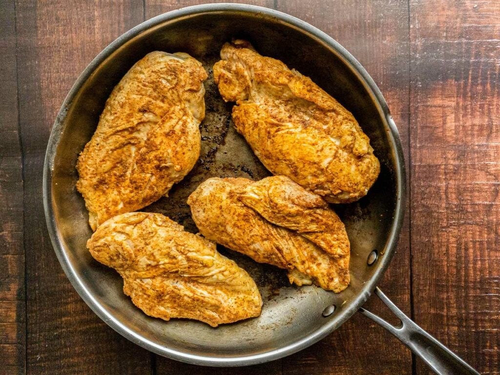 Four chicken breasts in a frying pan.