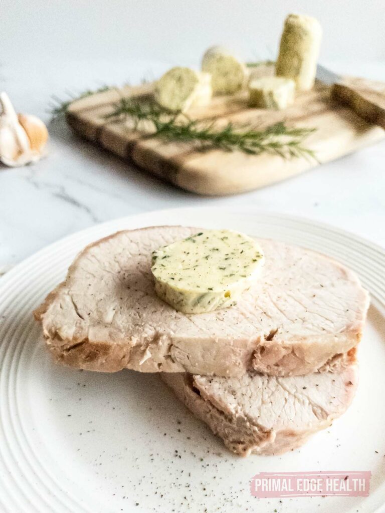 A slice of rosemary garlic butter slice on top of meat.
