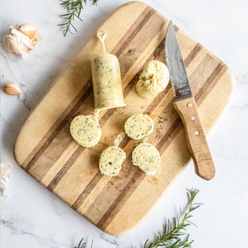 slices from a roll of rosemary garlic butter with rosemary sprigs