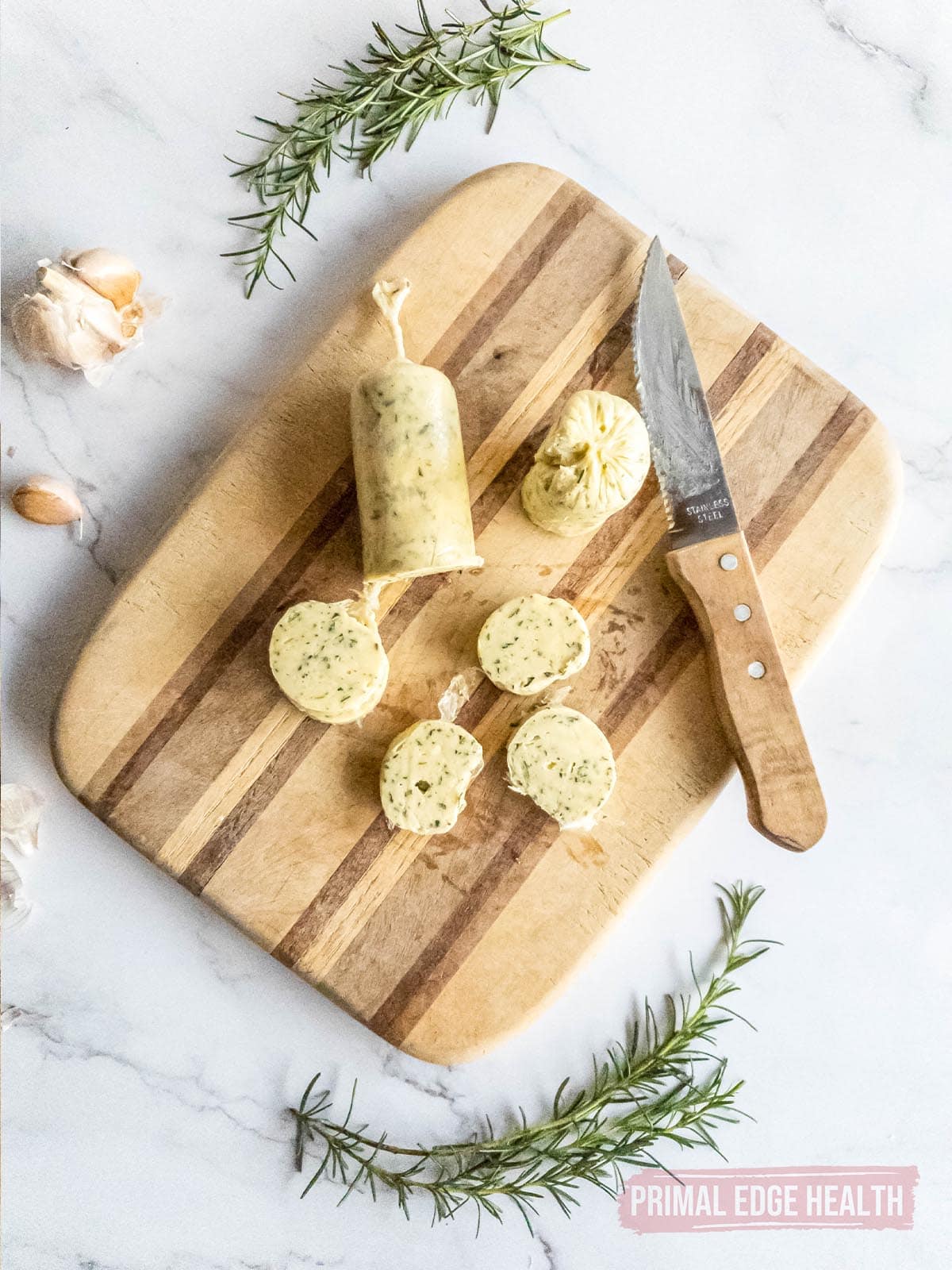 Slices from a roll of rosemary garlic butter on wooden board with a knife.