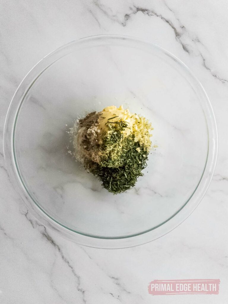 A glass bowl containing various herbs and spices on a marble surface.