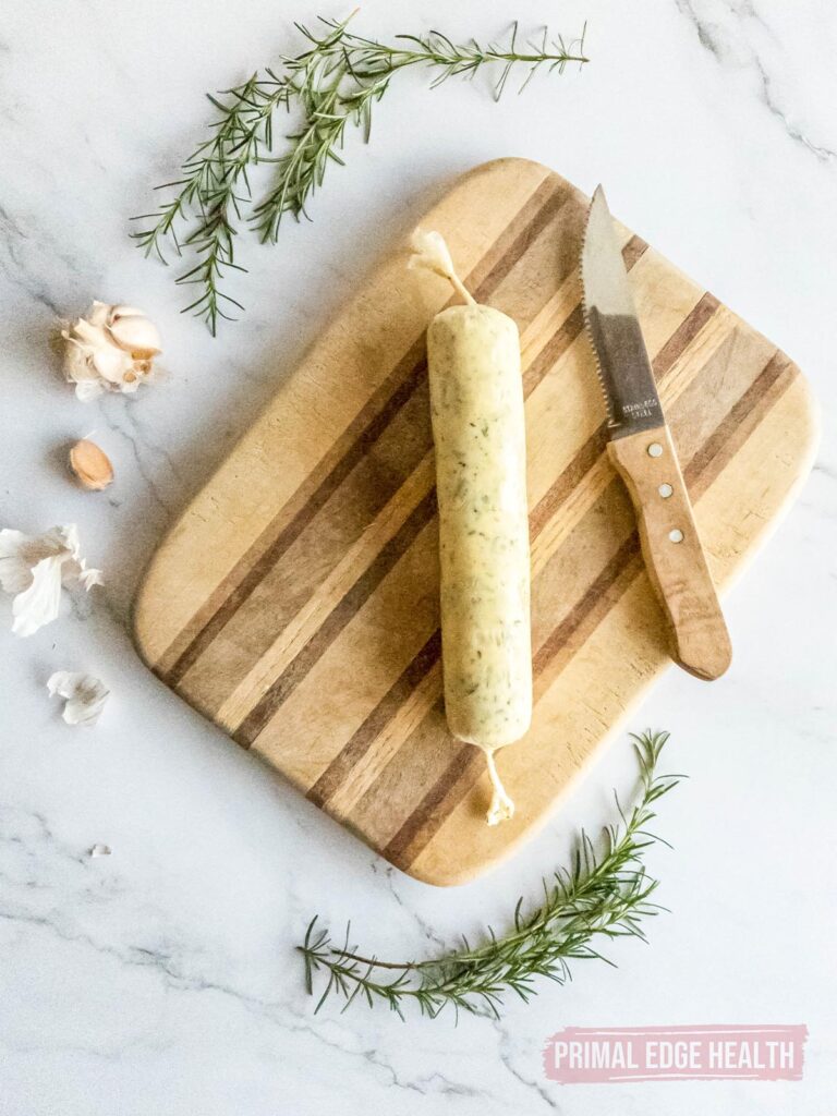A roll of rosemary garlic butter on cutting board with knife.