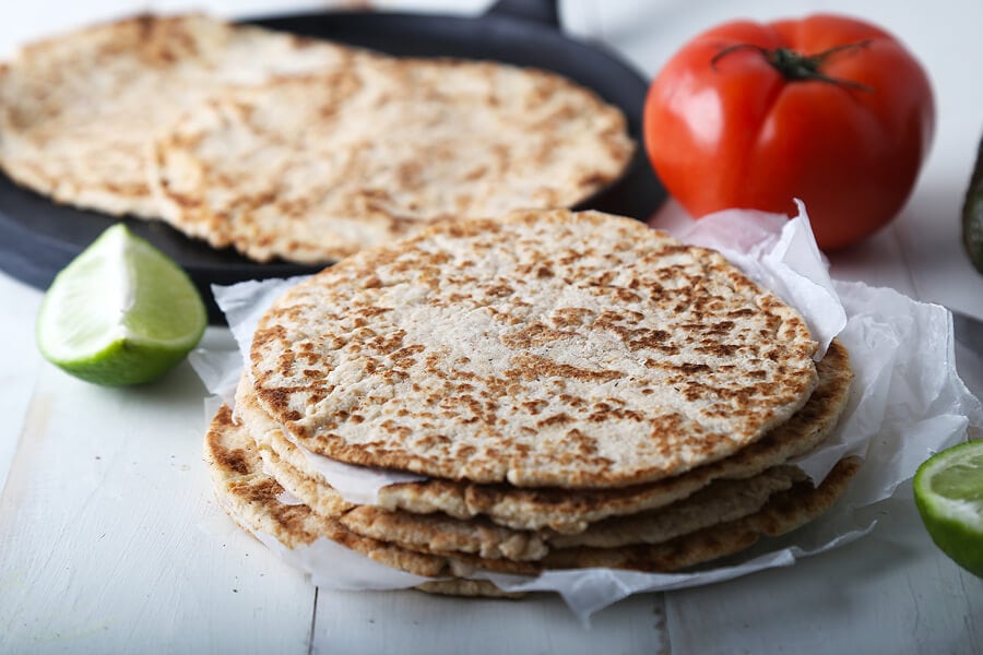 Keto tortillas stacked on a plate beside a tomato and lime, supplemented with keto-friendly psyllium husk.