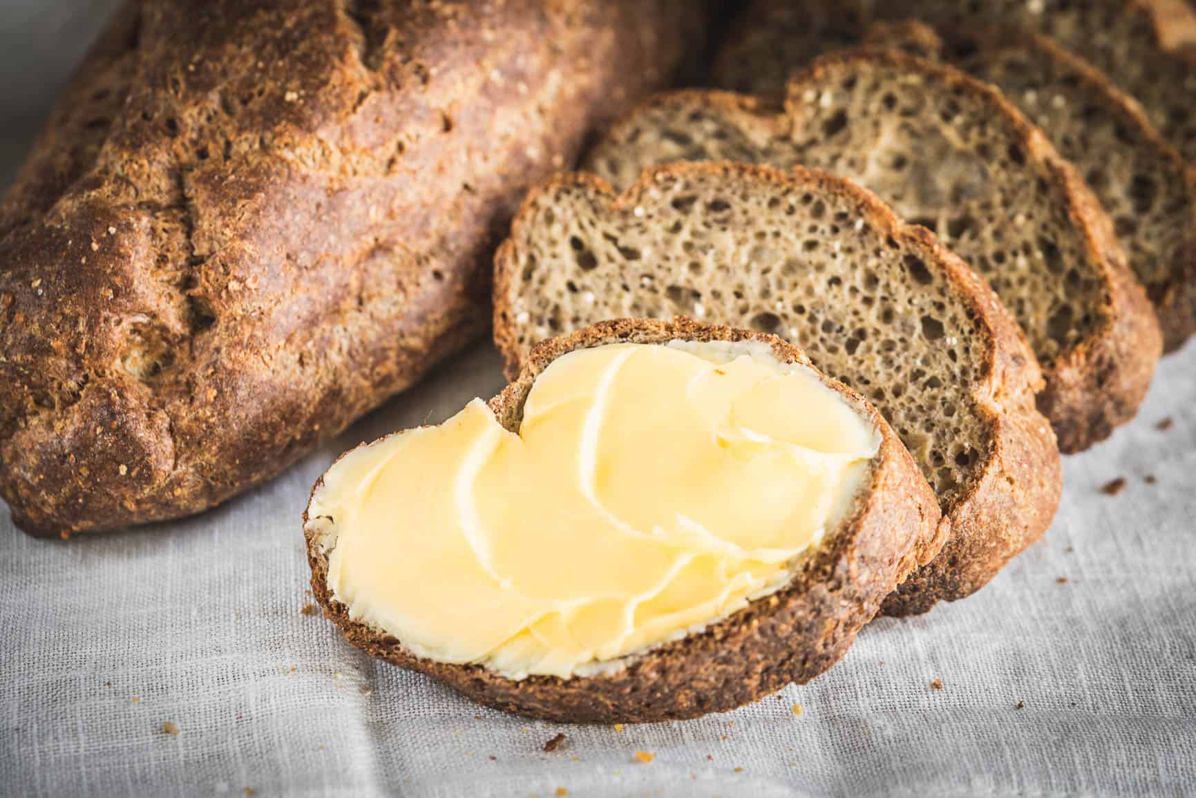 Sliced pieces of bread with one piece topped with butter.