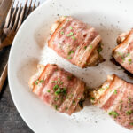 Four chicken thighs wrapped in bacon on plate on cutting board.