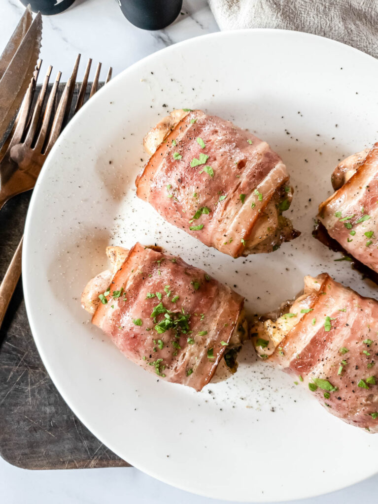 Four chicken thighs on plate on cutting board with salt and pepper shakers.