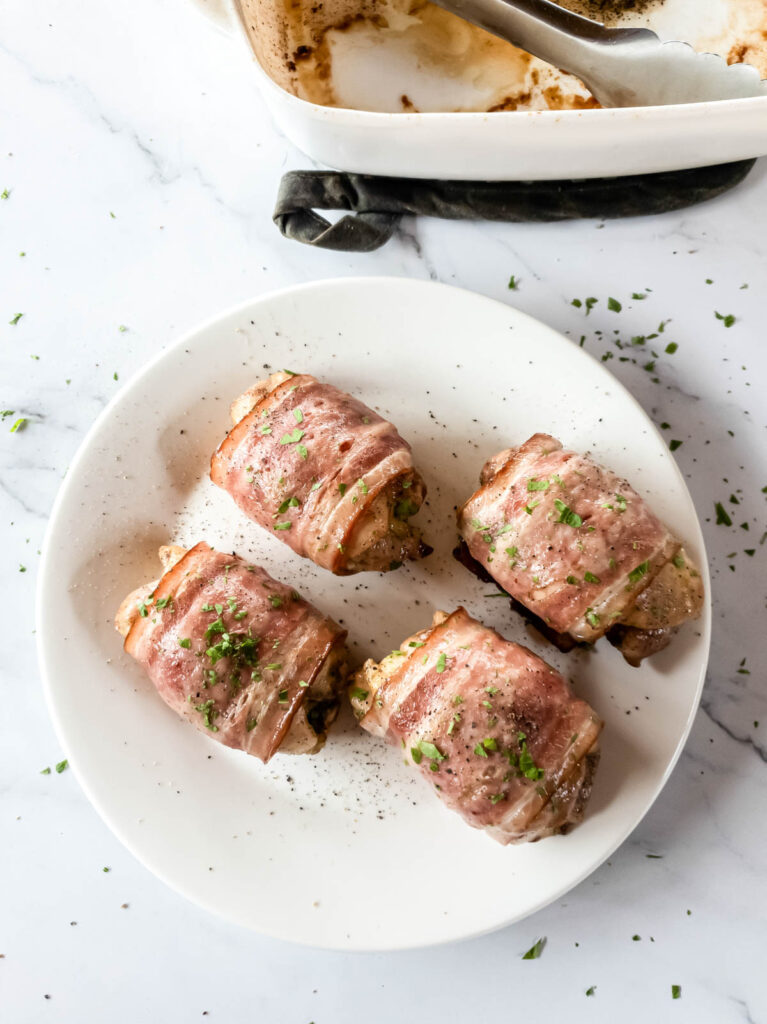 Four bacon wrapped chicken thighs with garnish on a plate.