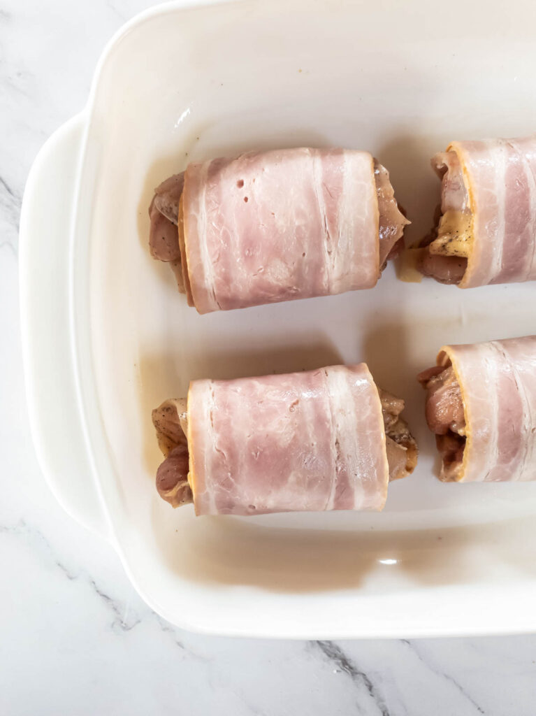 Bacon wrapped chicken thighs ready to go in the oven in baking dish.