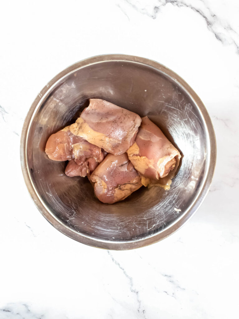 Raw chicken thighs seasoned with salt and pepper in a bowl.