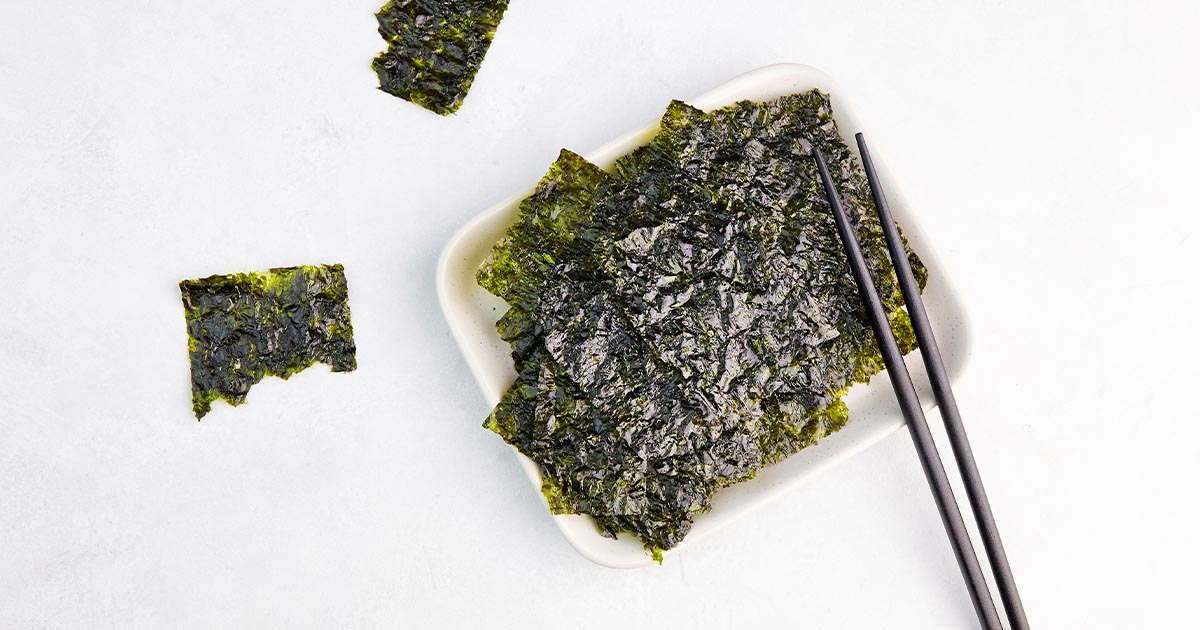 Toasted seaweed in a white bowl with chopsticks.