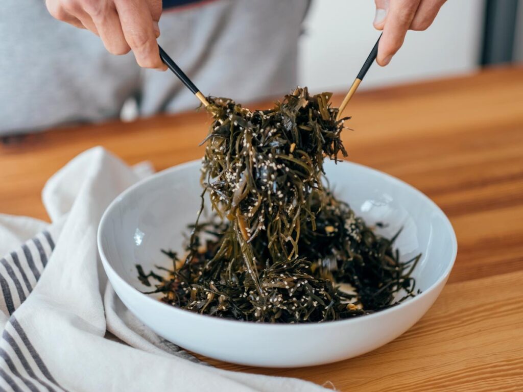 Tossing seaweed salad in a bowl with chopsticks.