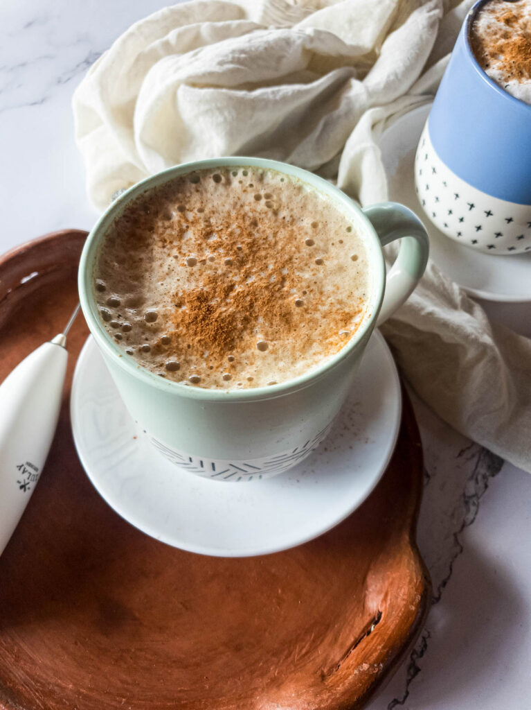 Milk frother next to latte in sea foam ceramic mug in saucer with tray.