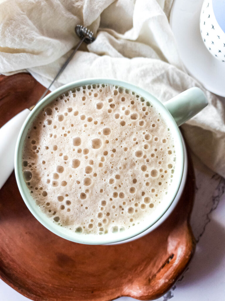 Frothed milk on coffee with milk frother to the side.