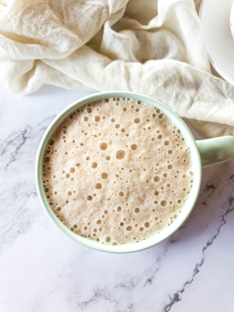 Frothed milk poured over sweetened ashwagandha coffee in mug.