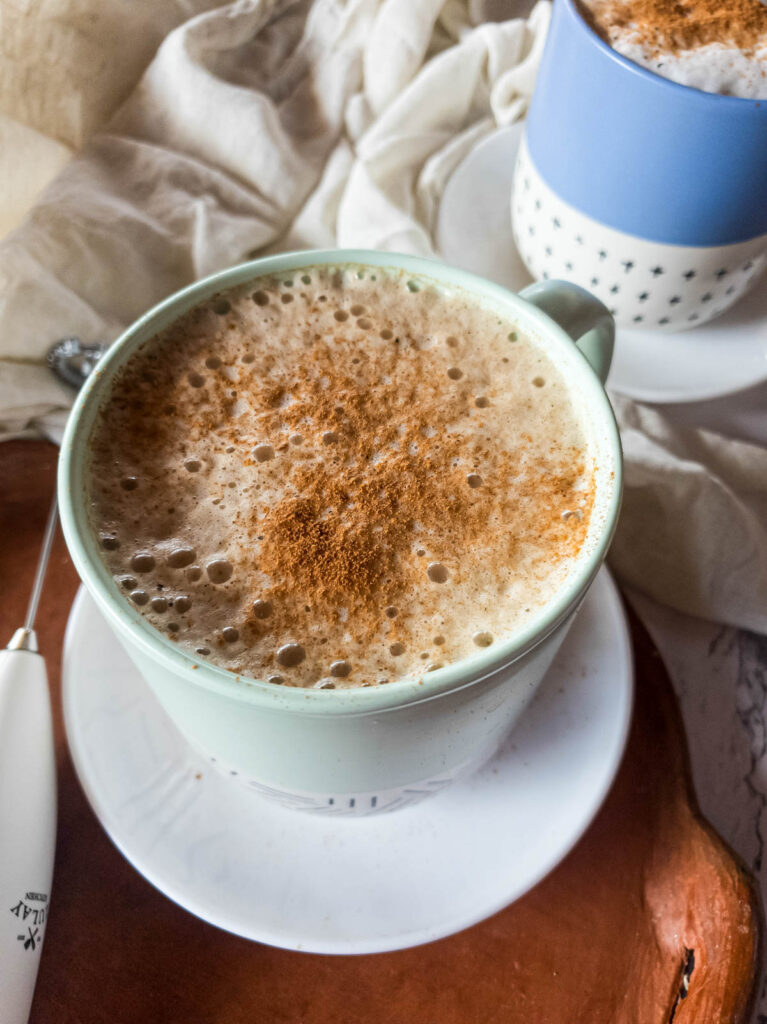 Cinnamon dusted top of hot latte in mug on saucer and serving tray.