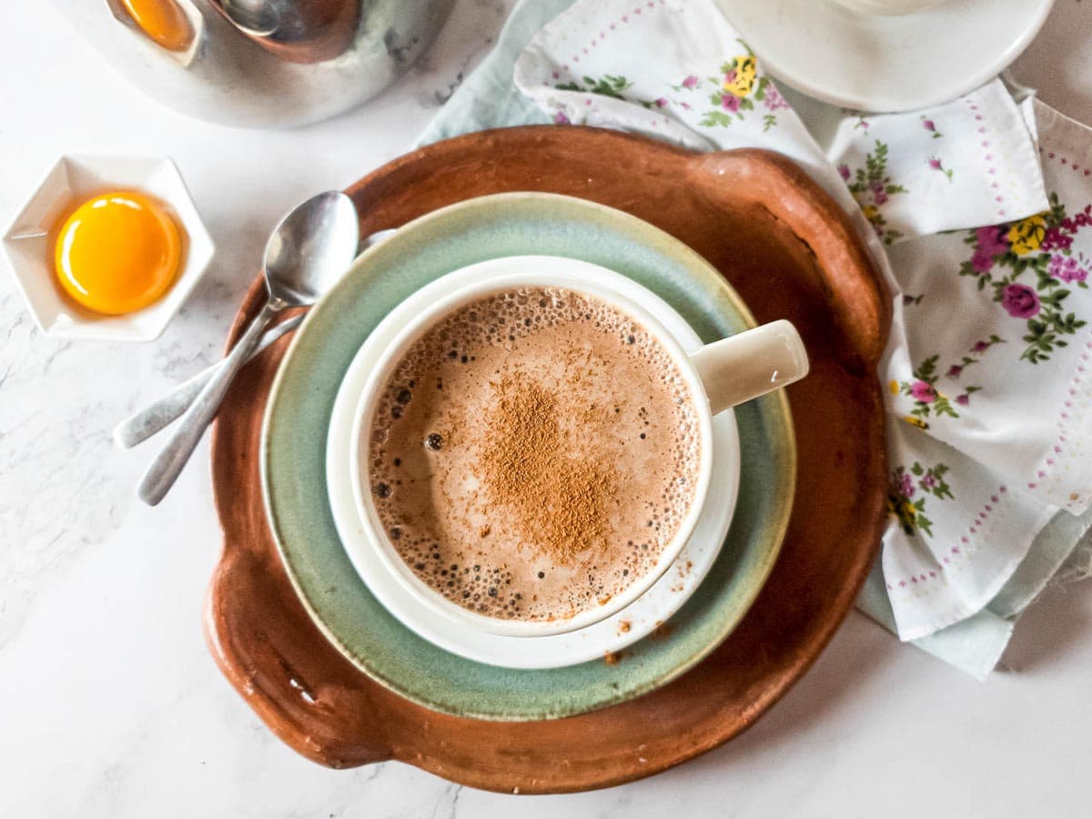 A picture of bone broth latte with pretty cloth and egg yolk in background.