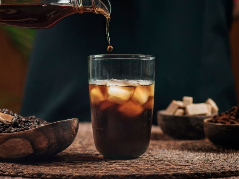 An iced coffee being poured into a glass.