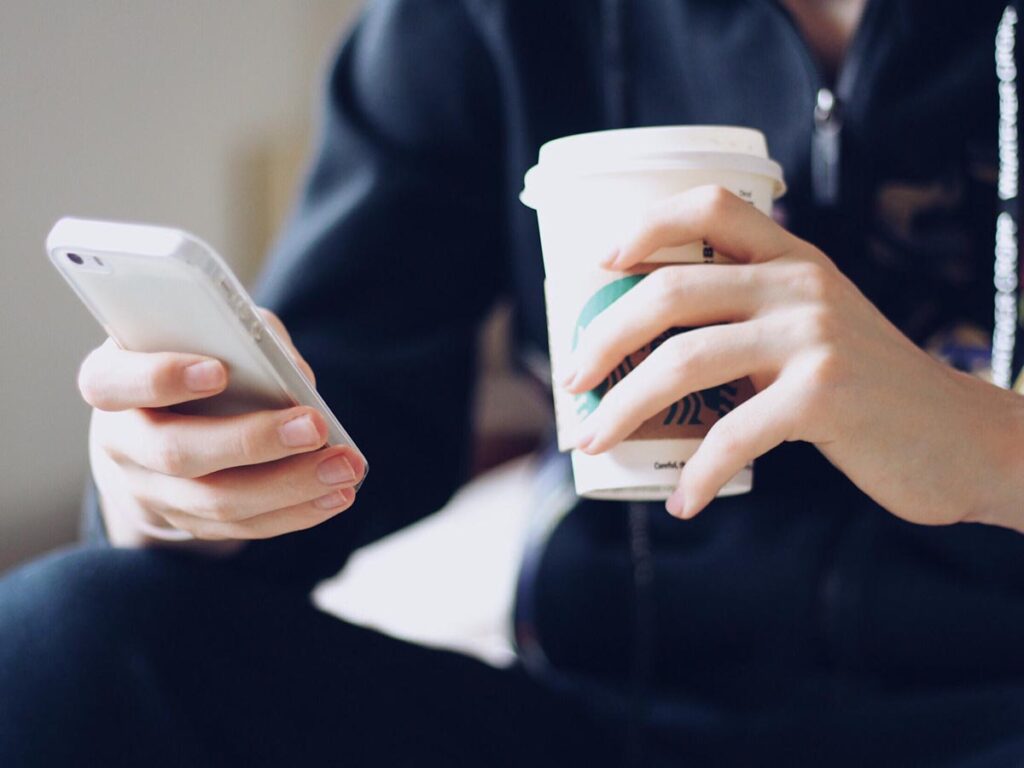 A person holding a cup of sugar-free Starbucks coffee and a cell phone.