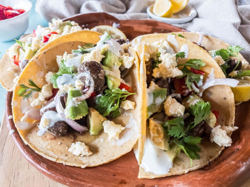 Horizontal picture showing beef heart tacos with toppings on a ceramic plate.