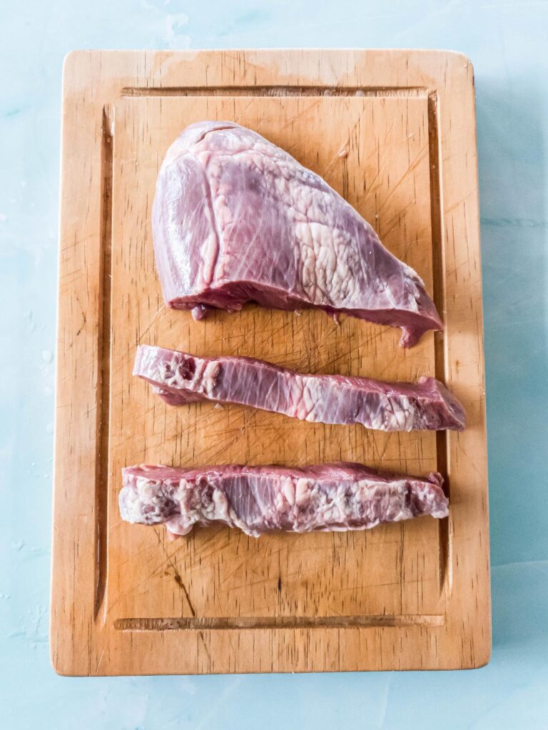 Uncooked beef heart slices on wooden cutting board.