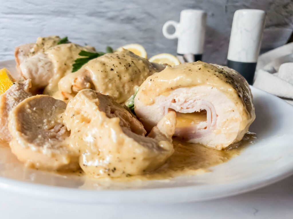 A picture of keto chicken cordon bleu cut in slices on white plate with sauce.