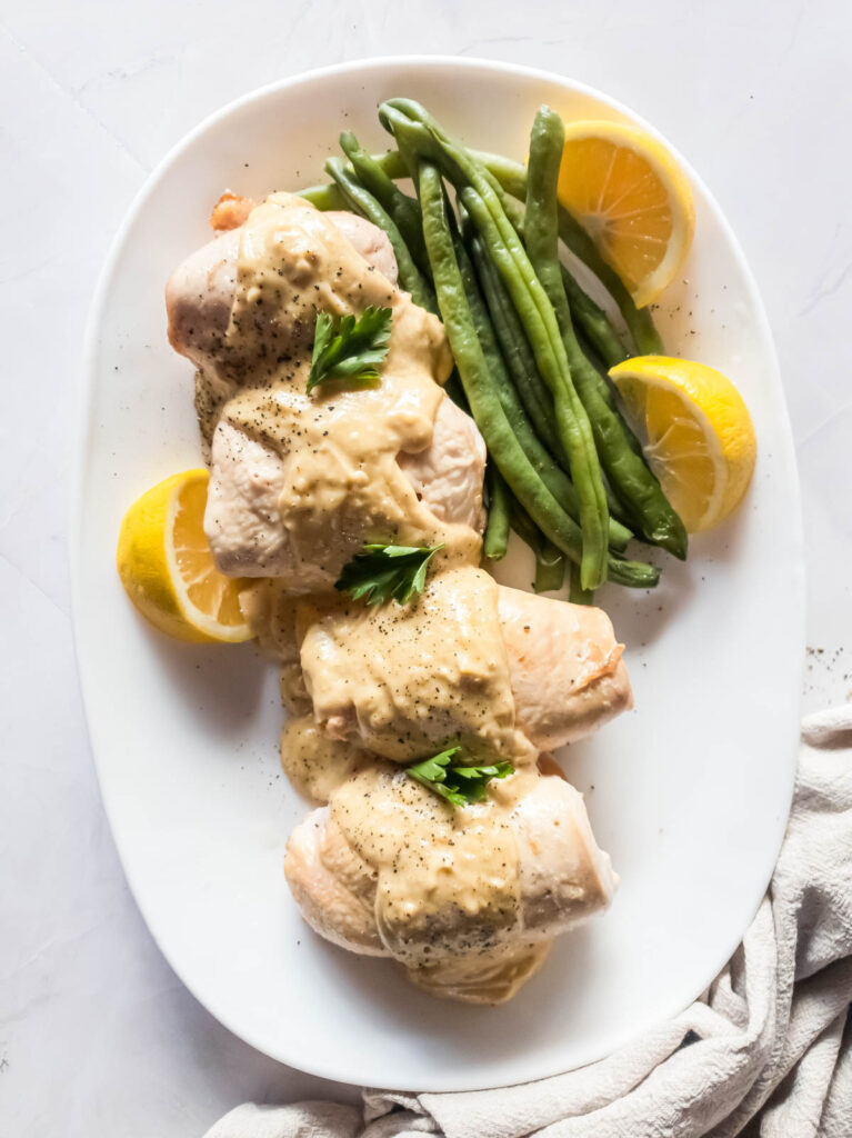 Chicken breasts with lemon wedges and sauce with green beans on a white plate.
