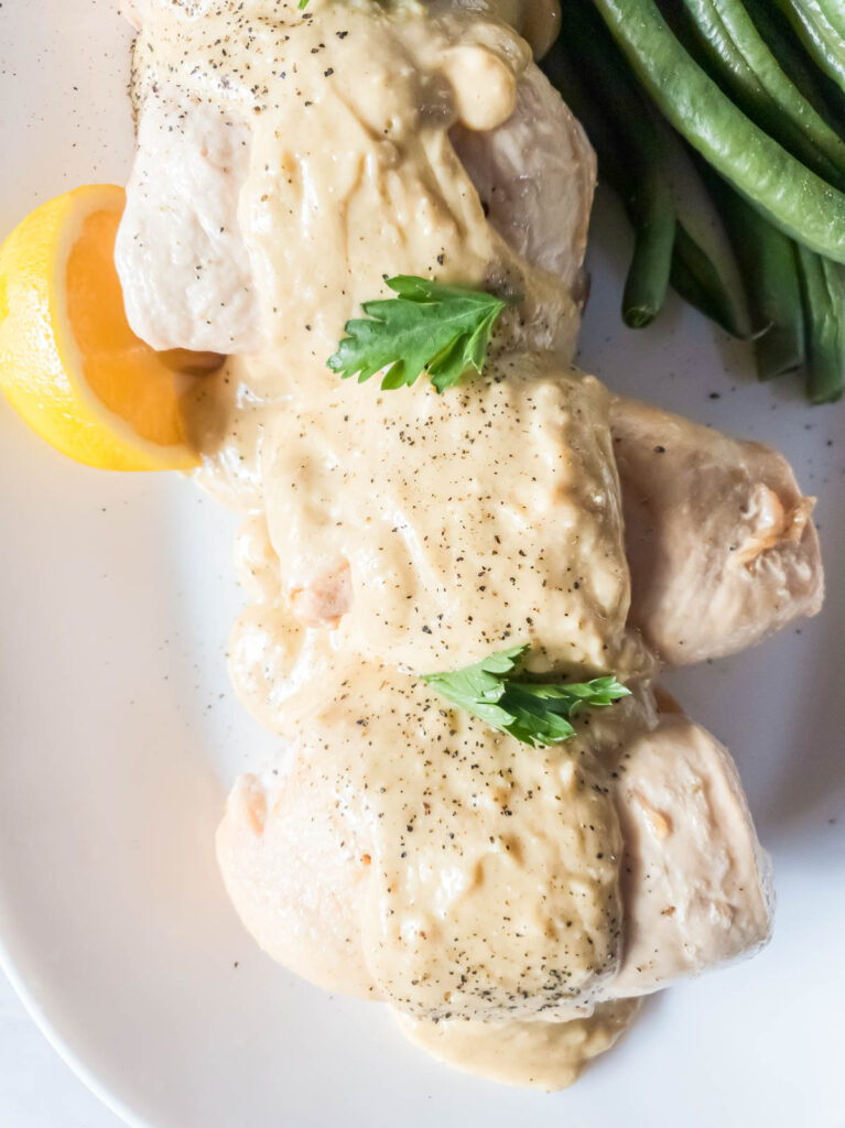 Ham and Swiss cheese stuffed chicken breasts with alfredo sauce and parsley garnish on a white plate.