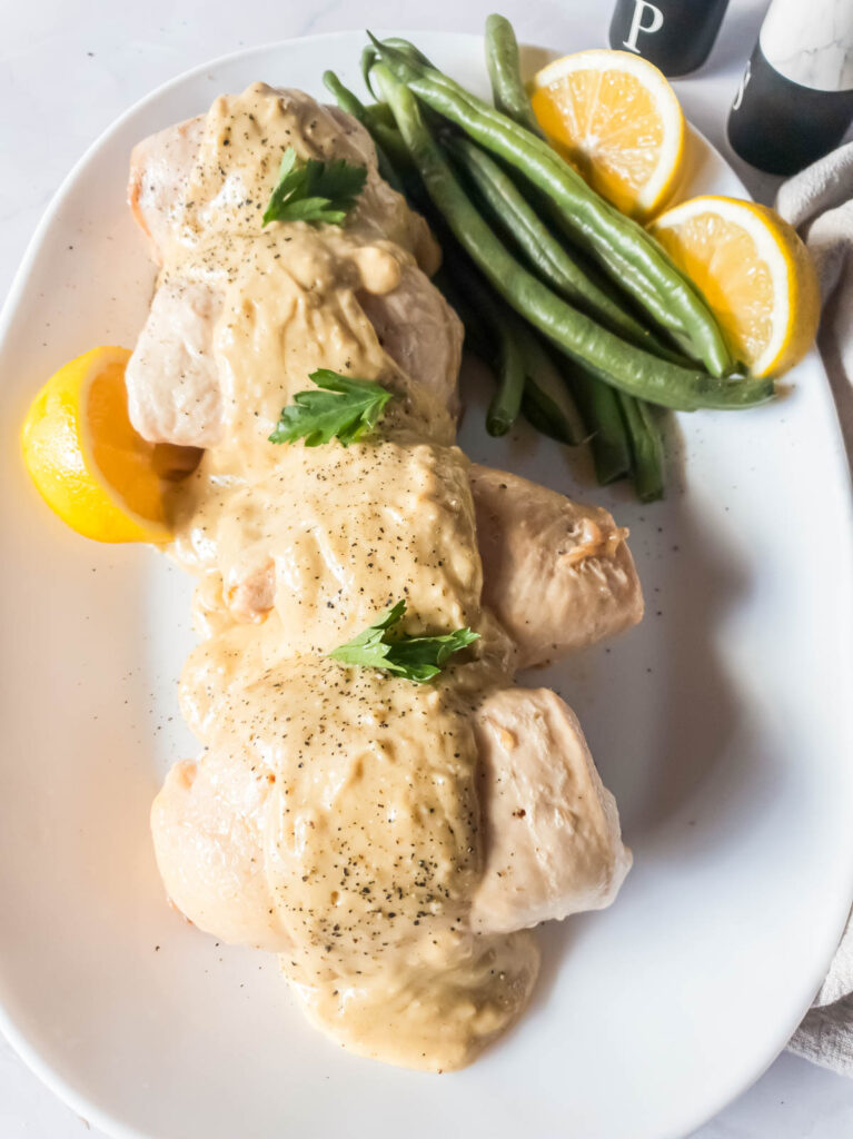 Stuffed chicken breasts with alfredo sauce and green beans on white plate.