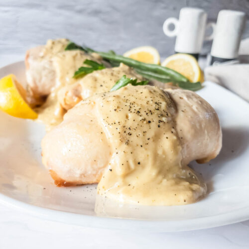 Chicken breasts with alfredo cheese sauce on a white plate.