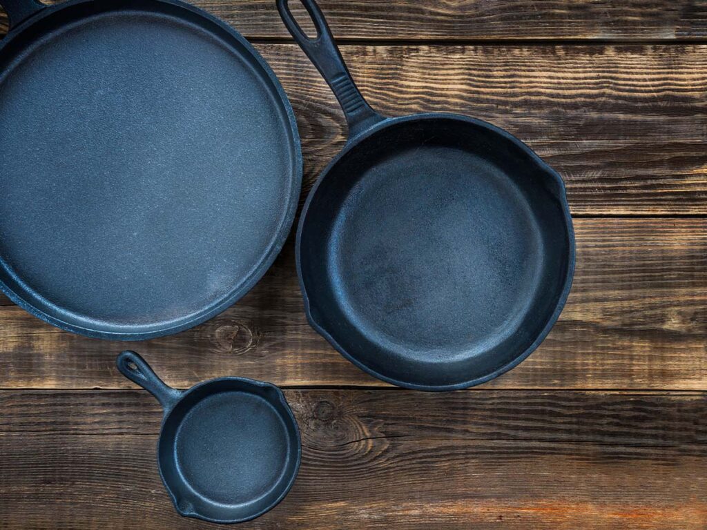 Three cast iron skillets on a wooden table.