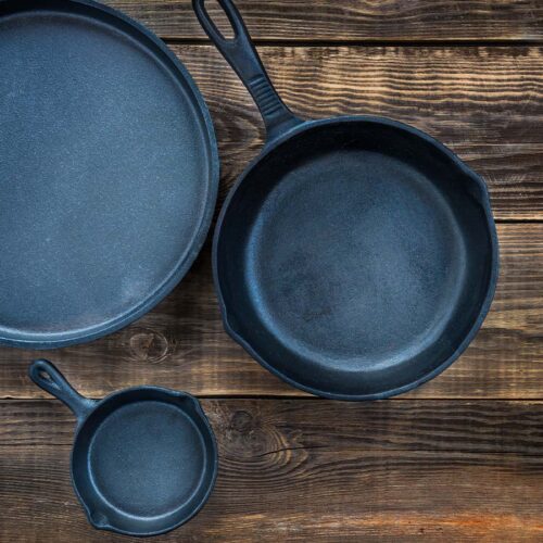 Three cast iron skillets on a wooden table.