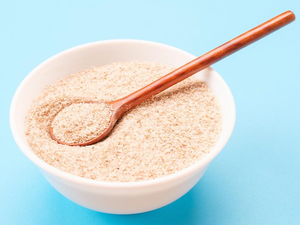 A bowl of psyllium husk with a wooden spoon on a blue background.