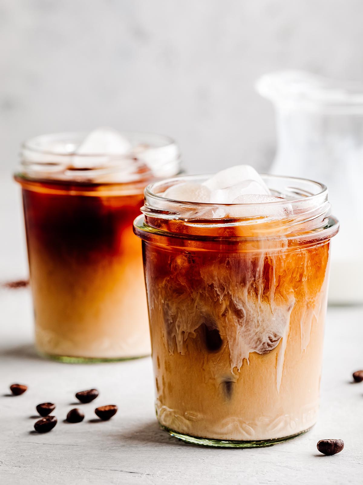 Two jars of iced coffee with cream and coffee beans.